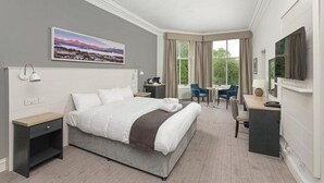A modern hotel room with a large bed, a desk, a chair, a TV, and a painting on the wall. - Tarbet Hotel (Arrochar)