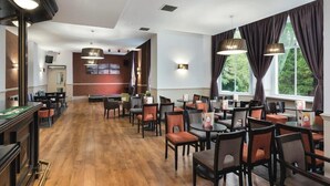 A spacious hotel dining area with multiple tables and chairs, large windows with curtains, and a wooden floor. - Tarbet Hotel (Arrochar)