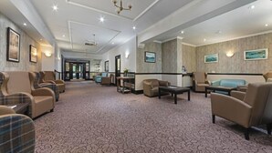 A spacious lobby with a patterned carpet, leather sofas, and a chandelier. - Tarbet Hotel (Arrochar)