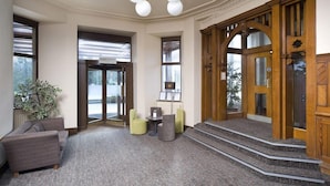 A lobby with a grey carpet, a grey sofa, a green armchair, a small table, and a staircase leading to an entrance. - Tarbet Hotel (Arrochar)