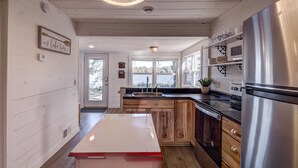A modern kitchen with wooden cabinets, stainless steel appliances, and large windows offering views of the outdoors.