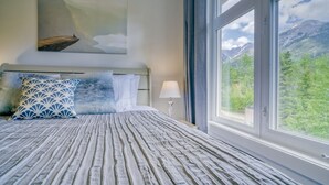 Un letto con copriletto a righe, un quadro che raffigura un paesaggio montuoso e vista sul verde attraverso ampie finestre.