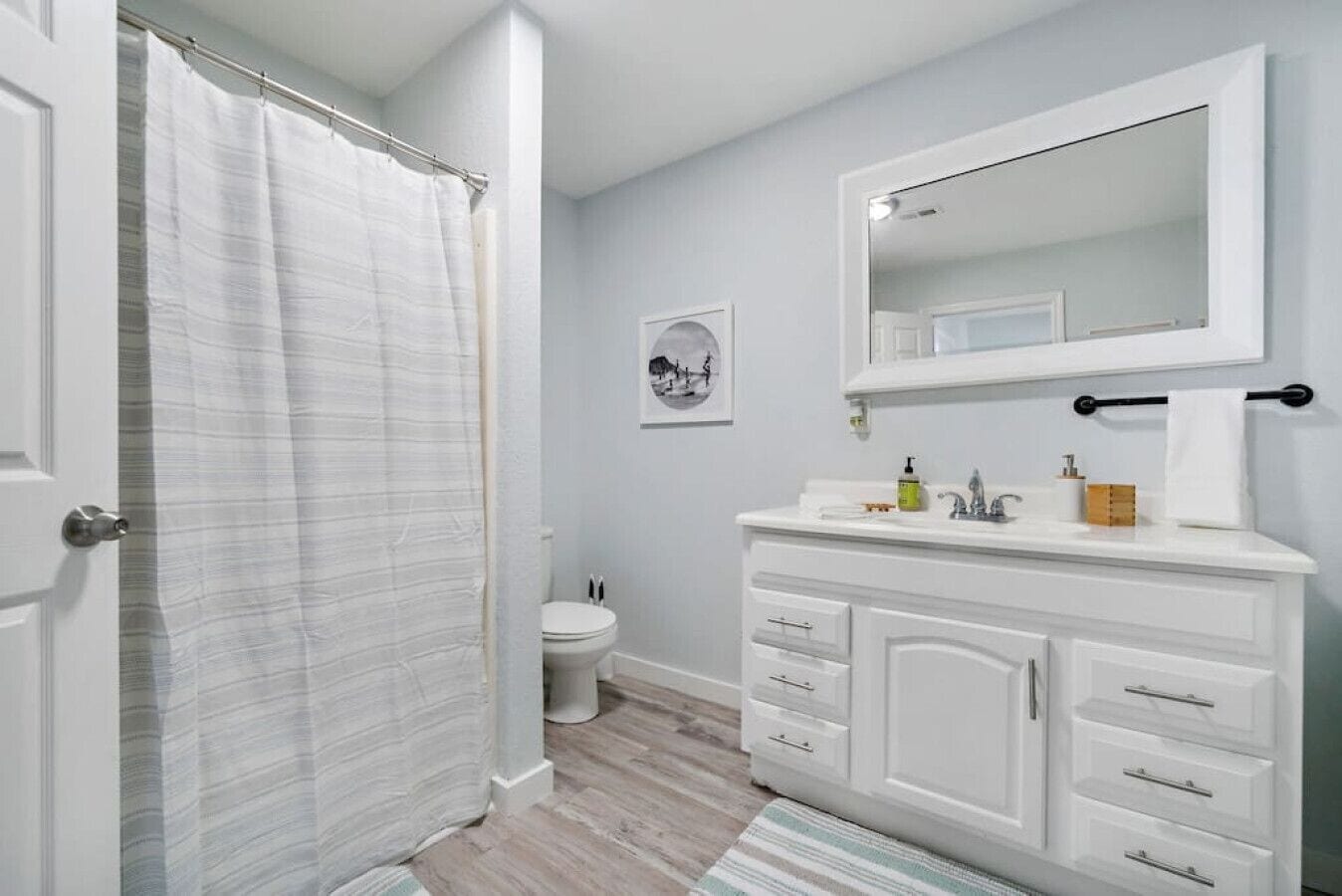Ein Badezimmer mit Duschvorhang, Toilette, Waschbecken mit Spiegel und einem gerahmten Bild an der Wand.