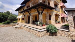 A two-story house with stone and stucco exterior, multiple balconies, and a gravel driveway. - Casa nel Bosco con Sauna (Cervasca)
