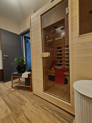 Una sauna con paredes de madera y puerta de vidrio, una mesita con una planta y una toalla roja en el banco.