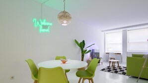 Un espace repas moderne avec un néon, une table ronde, des chaises vertes et une grande plante.