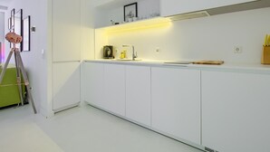 Une cuisine moderne avec des meubles blancs, un four encastré et un plan de travail sur lequel se trouvent une bouilloire et une machine à café.