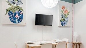 Een eetgedeelte met een tafel, stoelen, een televisietoestel en kunstwerken aan de wanden.