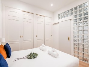 A hotel room with a bed, two doors, a glass block wall, and a lamp.
