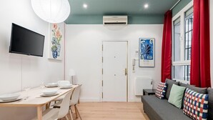 Een moderne woonkamer met een eethoek, een flatscreen televisie, een plafondventilator en een raam met rode gordijnen.