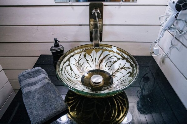 Ein Badezimmer mit einem Waschbecken aus Glas, einem Handtuch und einem Fön.