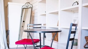 A dining area with a round table, two red cushioned chairs, a metal-framed mirror, and white shelving units. - Granary Two Bedroom Luxury Suite (Dallas)