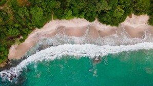 An aerial view of a beach with clear turquoise waters and a sandy shore.