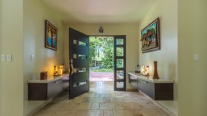 A hallway with a door leading to an outdoor area, flanked by two side tables with decorative items and framed artwork on the walls.