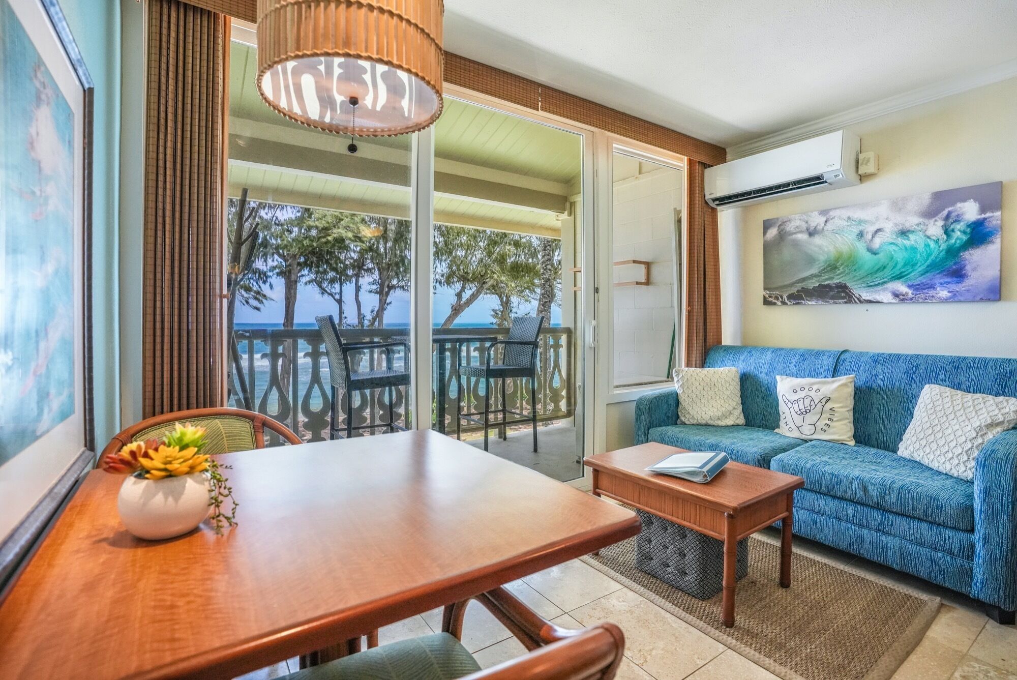 A room with a wooden table, a blue sofa, and a balcony with a view of the ocean.