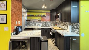 A modern kitchen with dark cabinetry, a tiled backsplash, and a countertop with a built-in microwave and ice dispenser.