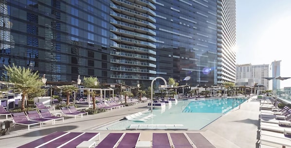 A rooftop pool area with lounge chairs and a swimming pool, surrounded by high-rise buildings.