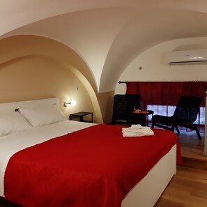 Ein Hotelzimmer mit einem großen Bett, einem kleinen Tisch, einem Stuhl und einem Fenster mit Vorhängen.