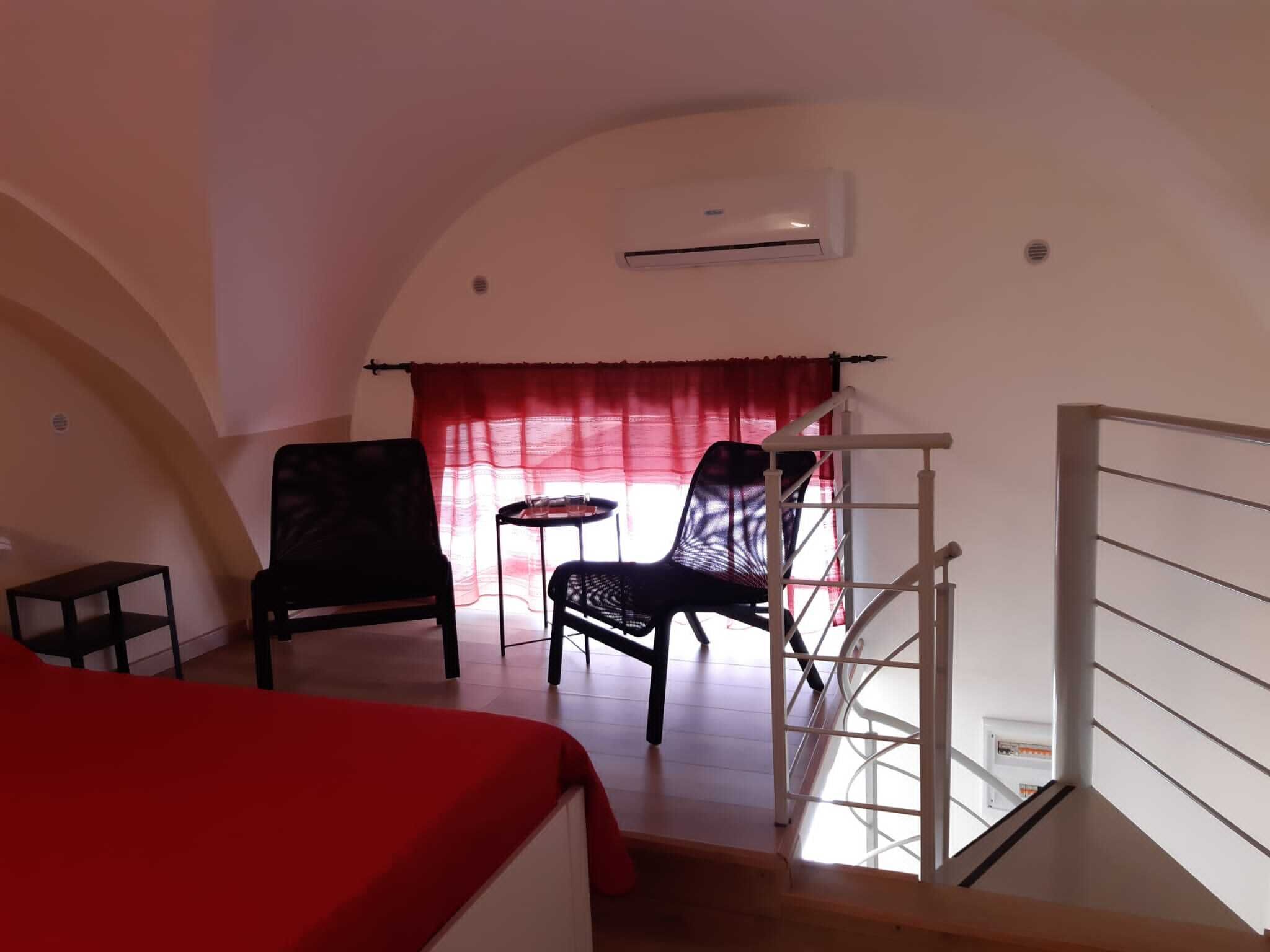 Une chambre à coucher avec un lit, une chaise, une petite table et une fenêtre avec un rideau rouge.