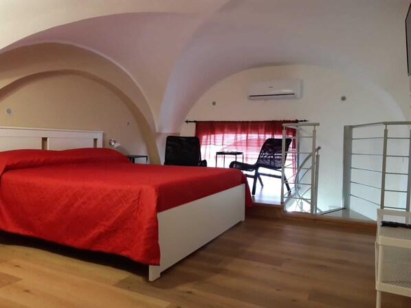 Ein Schlafzimmer mit Bett, Stuhl, Schreibtisch und einem Balkon.