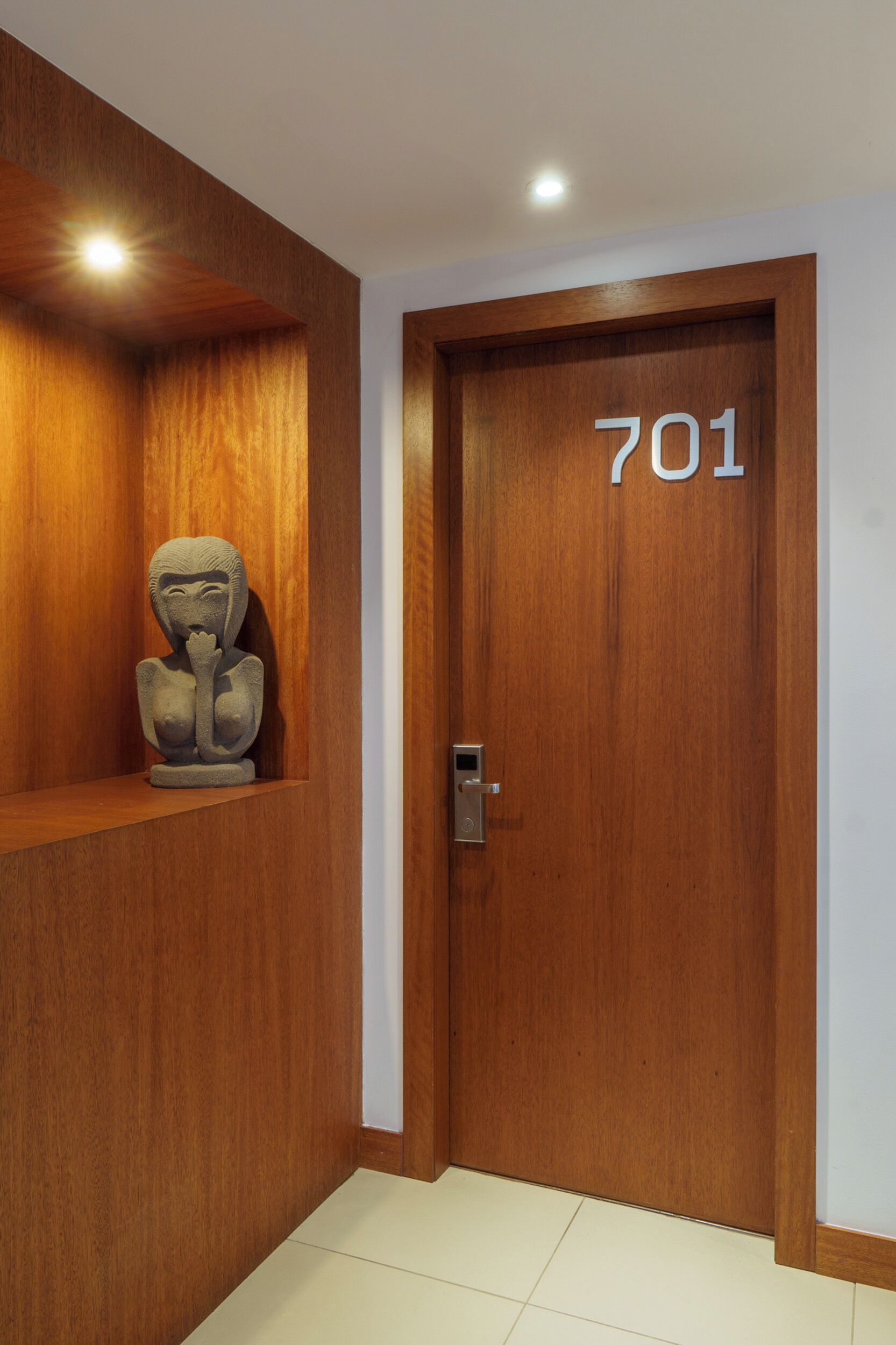 A wooden door with the number 701, a small statue on a shelf, and a recessed ceiling light.