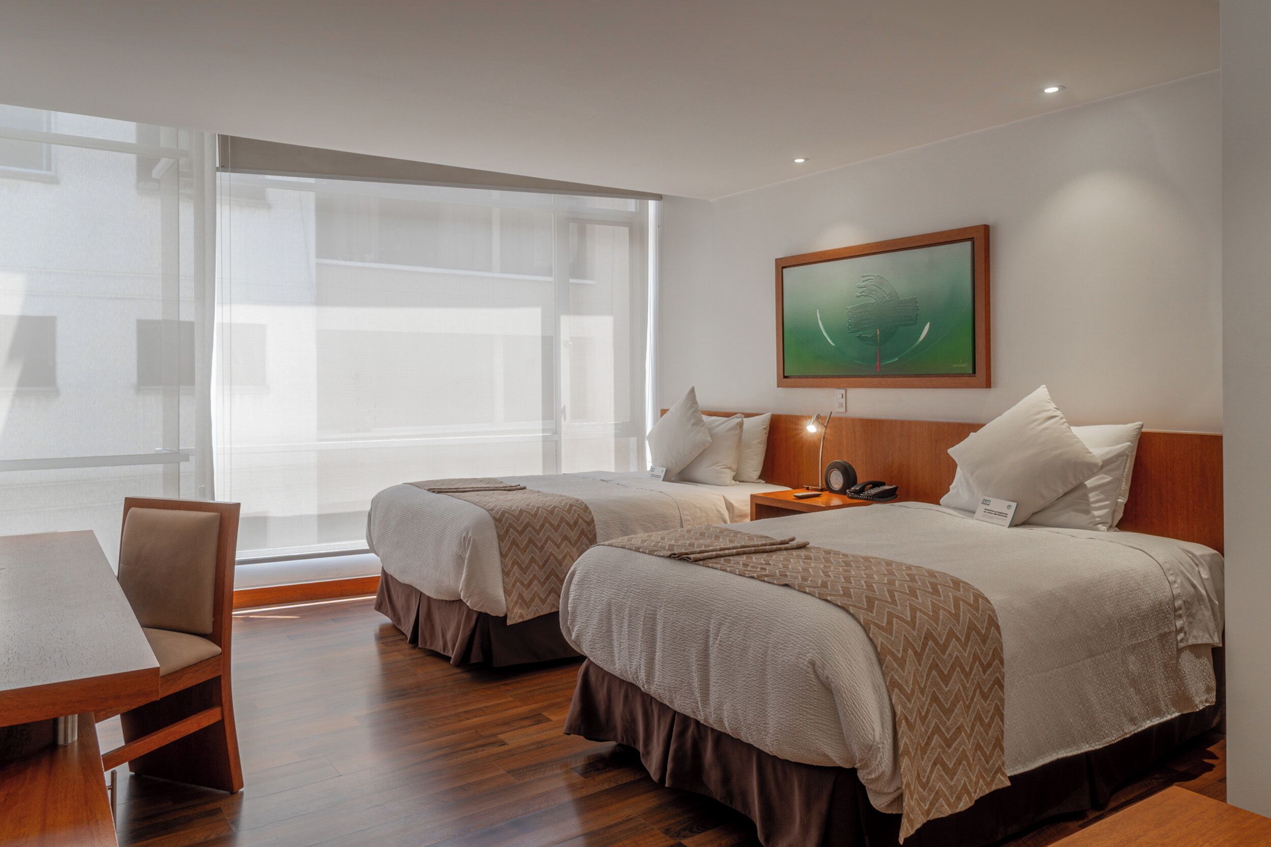 Habitación de hotel con dos camas, una mesa de madera y un ventanal grande.