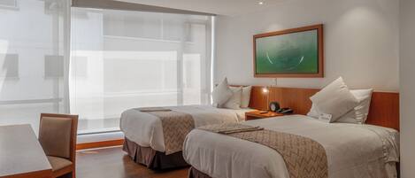 Habitación de hotel con dos camas, una mesa de madera y un ventanal grande.