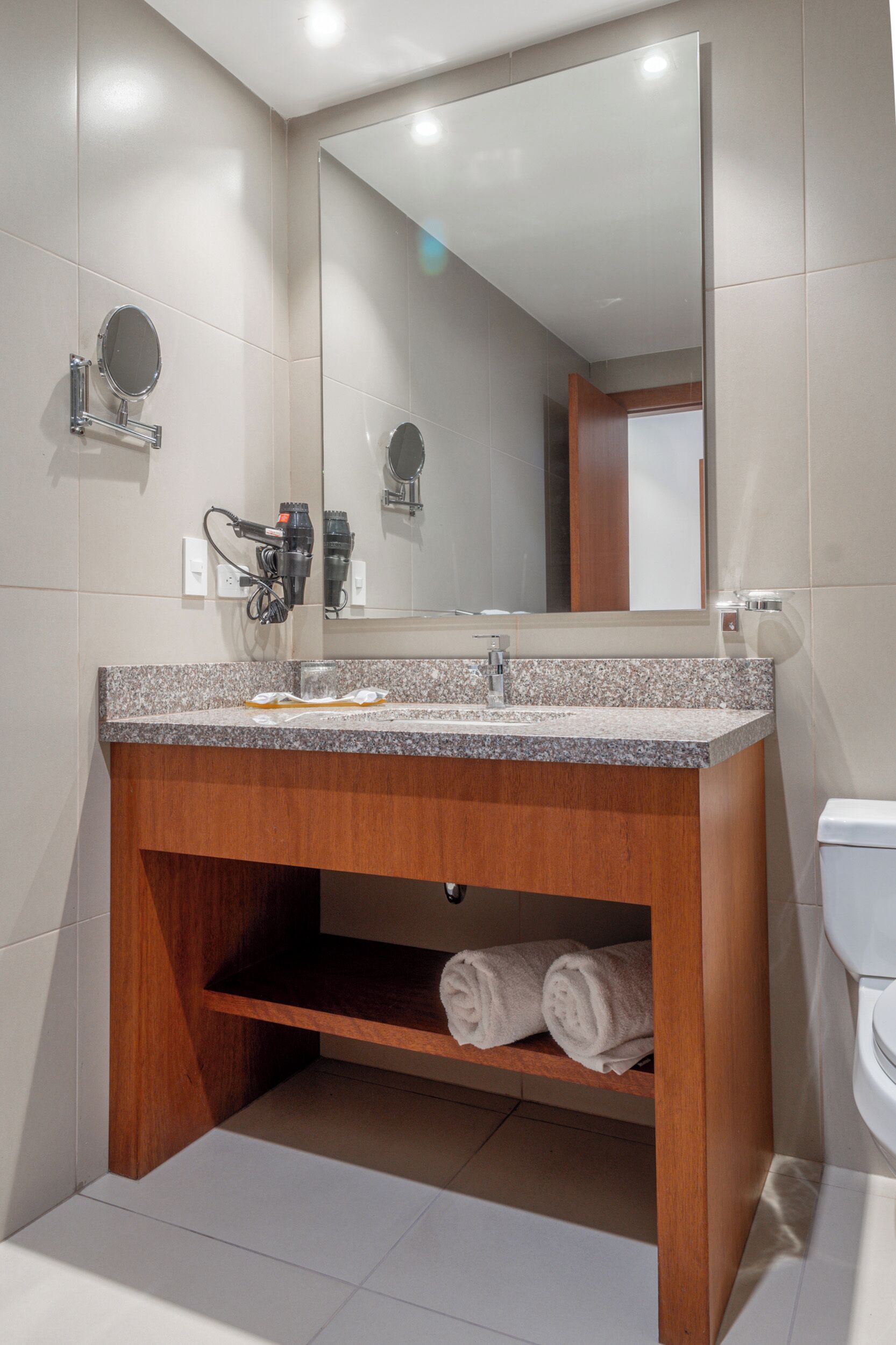 A bathroom with a granite countertop sink, a mirror, and a wooden vanity.