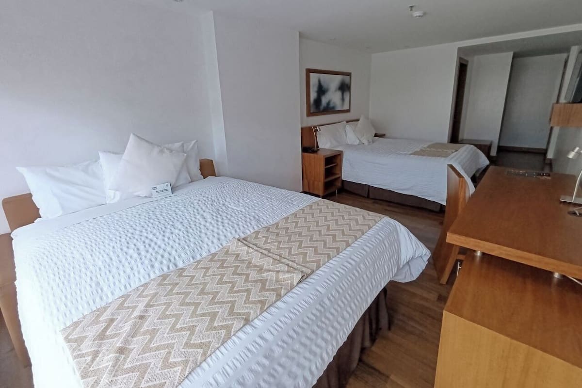 A hotel room with two beds, a wooden desk, and a small cabinet.