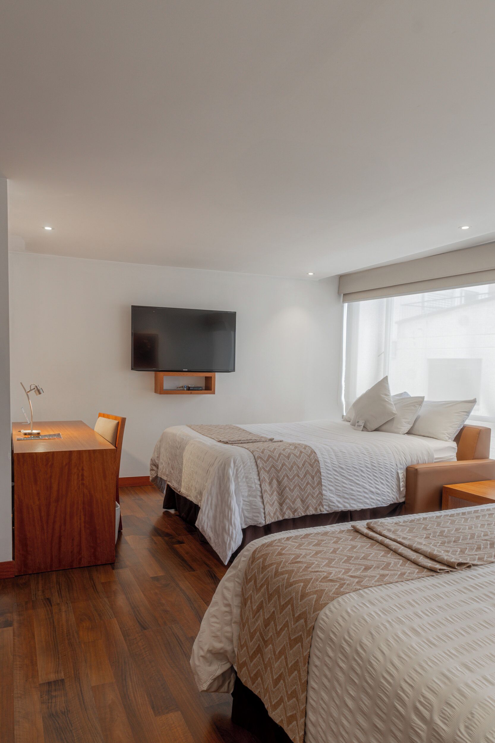 Une chambre d’hôtel avec deux lits, un téléviseur fixé au mur, un bureau et une fenêtre avec des rideaux.