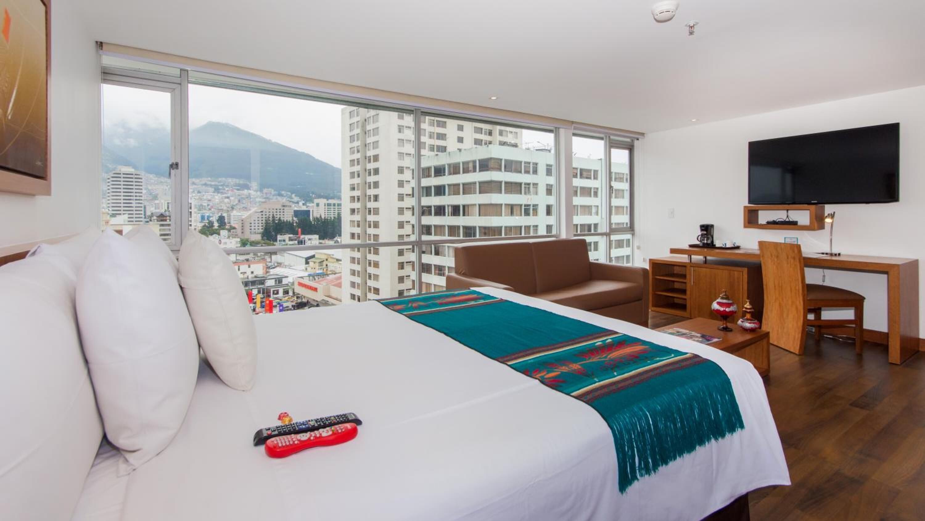 Habitación de hotel con una cama grande, un escritorio, una silla, un televisor y vistas a la ciudad.