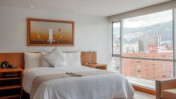 Una habitación de hotel moderna con una cama grande, piso de madera, vista a la ciudad y un cuadro en la pared.