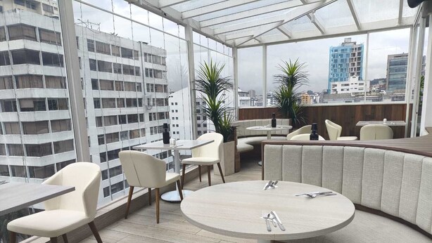 A modern rooftop bar with round tables and cushioned seating, overlooking a cityscape. - Zen Hotel Quito (Quito)
