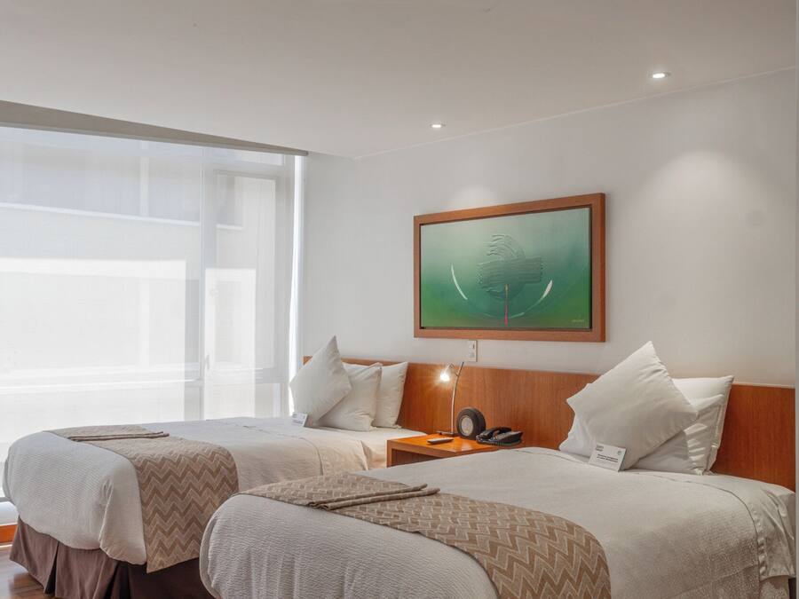 A hotel room with two beds, a large window, a painting on the wall, and a nightstand with a lamp.