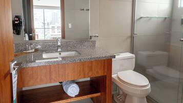 Un baño con encimera de granito, tocador de madera, inodoro blanco y mampara de vidrio.