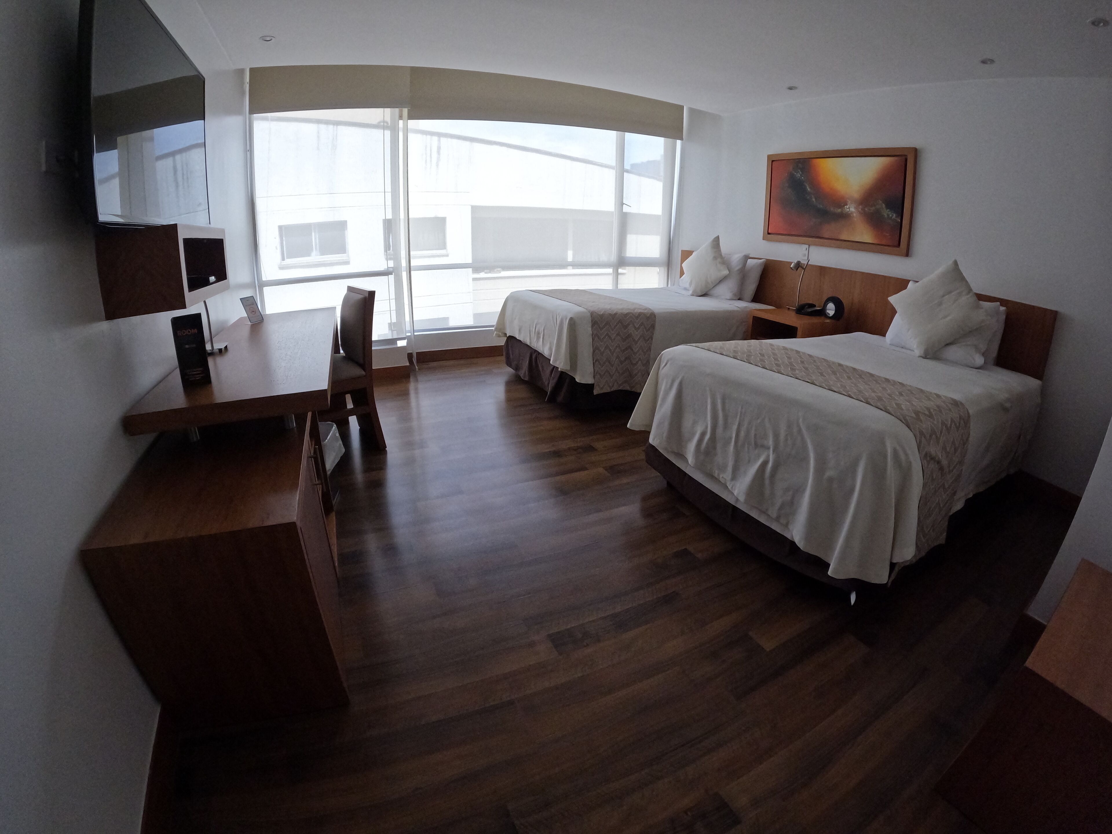 A hotel room with two beds, a desk, a chair, a TV, and a large window.