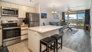 Una cocina moderna con electrodomésticos de acero inoxidable, una isla central con taburetes y un comedor con vistas al exterior.