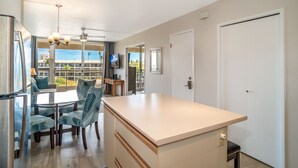 Una cocina moderna con una isla central, comedor con sillas y vistas al exterior.