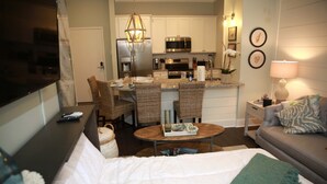 A hotel room with a bed, a dining area with wicker chairs, a kitchen with stainless steel appliances, and a living area with a sofa and lamp. - Luxury Condo at Village Pier, King Bed,Full Kitchen, Polaris Ranger for Rent (St. Simons Island)