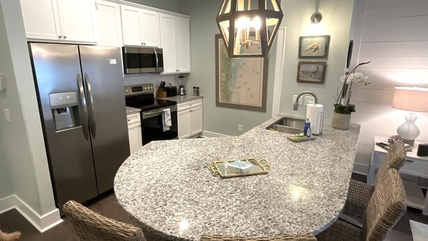 A kitchen with white cabinets, stainless steel appliances, a granite countertop, wicker chairs, and a pendant light. - Luxury Condo at Village Pier, King Bed,Full Kitchen, Polaris Ranger for Rent (St. Simons Island)