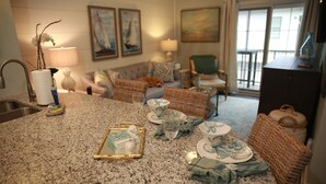 A kitchen with granite countertops, a dining area with wicker chairs, a sofa, and a dog. - Luxury Condo at Village Pier, King Bed,Full Kitchen, Polaris Ranger for Rent (St. Simons Island)