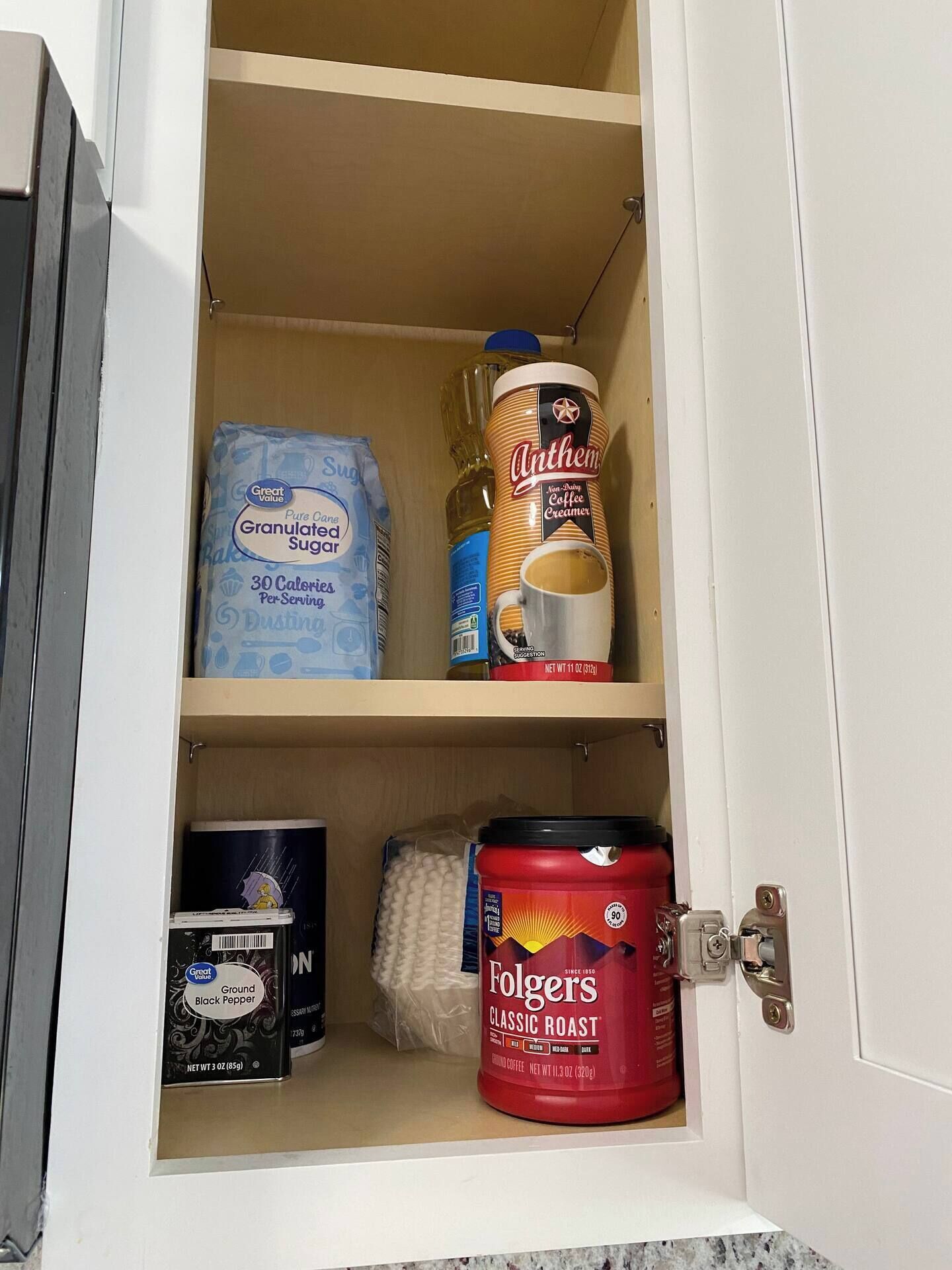 Un meuble avec des étagères contenant divers produits alimentaires, notamment du sucre en poudre, de la crème pour le café, du poivre noir moulu et du café Folgers Classic Roast.