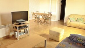 A living room with a TV, wooden dining table, chairs, a sofa, and an ottoman.