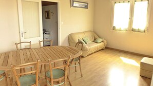 A room with a round wooden table and chairs, a beige sofa, and a window with curtains.