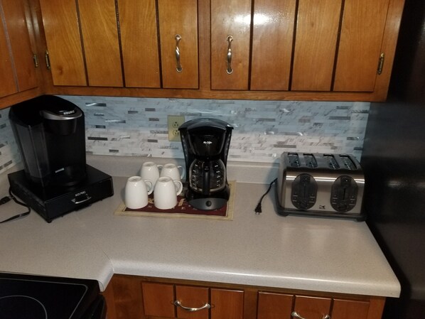 Une cuisine avec des meubles de rangement en bois, une machine à café, un grille-pain et six tasses blanches posées sur un tapis.