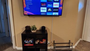 Televisão de tela plana fixada na parede, exibindo uma interface de serviço de streaming com diversos ícones de aplicativos.