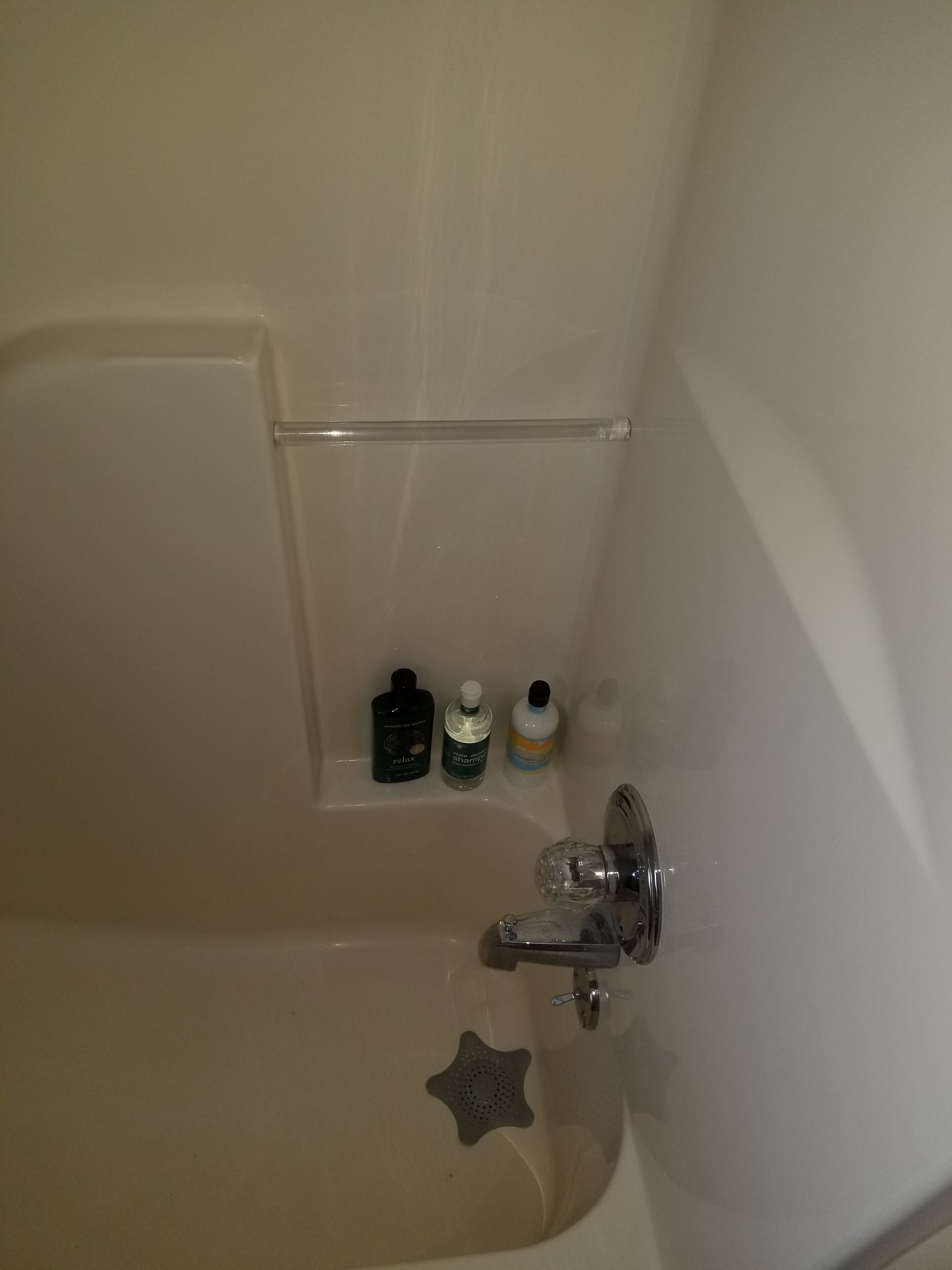 Una bañera con puerta de vidrio transparente, un cabezal de ducha y tres botellas de champú y acondicionador en la pared.