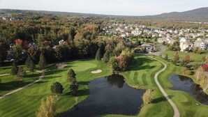 Um campo de golfe com um lago, rodeado por árvores e edifícios residenciais.