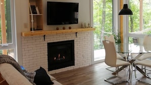 Uma sala de estar moderna com lareira, uma TV de tela plana e uma mesa de jantar de vidro.
