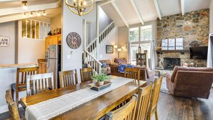 A spacious living area with a wooden dining table, comfortable seating, a stone fireplace, and a staircase leading to an upper level. - Dock, Boat Slip & View: Lakefront Tan-Tar-A Home! (Osage Beach)